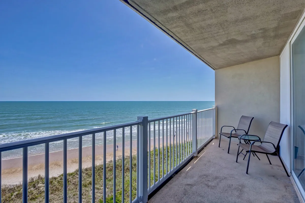 An exterior shot of a private balcony with comfortable seating, overlooking the sandy beach and the vast ocean. The setup is perfect for relaxing, reading, or enjoying sunrise and sunset with unobstructed water views.