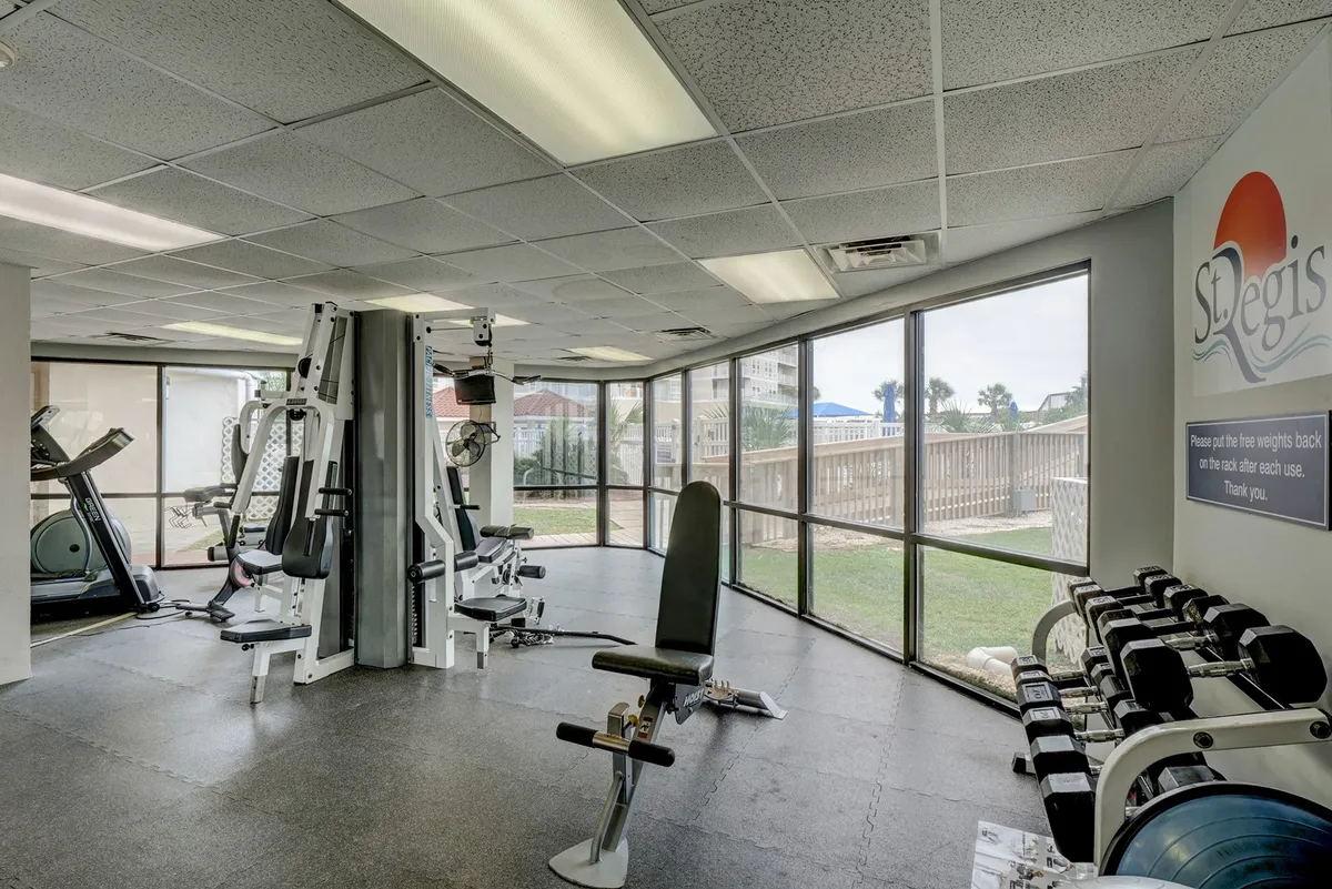 A bright, inviting fitness center with a variety of exercise machines, dumbbells, and large windows letting in ample daylight. The room is spacious, modern, and motivational, supporting both solo and group workouts.