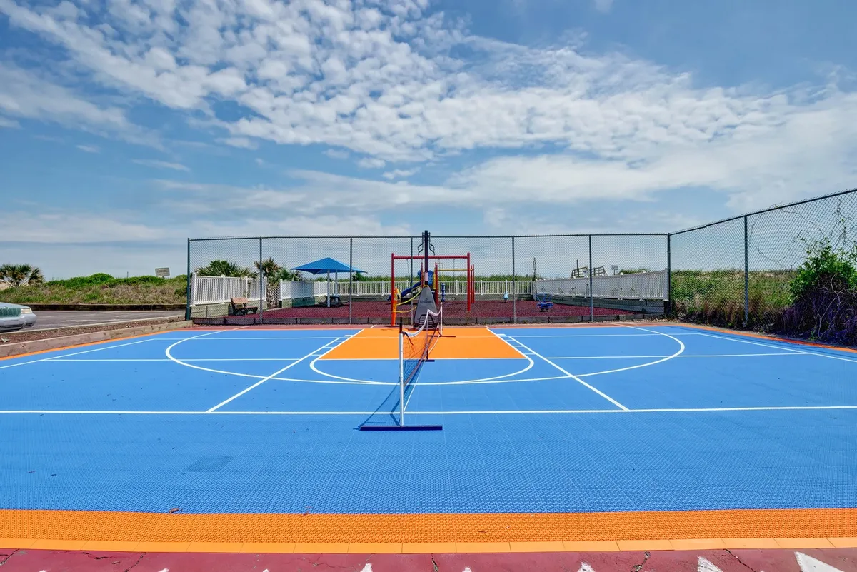 An exterior scene showing a vibrant basketball court, tennis net, and modern playground equipment surrounded by greenery. The active atmosphere hints at a family-friendly environment where guests can enjoy a variety of outdoor sports and recreation.