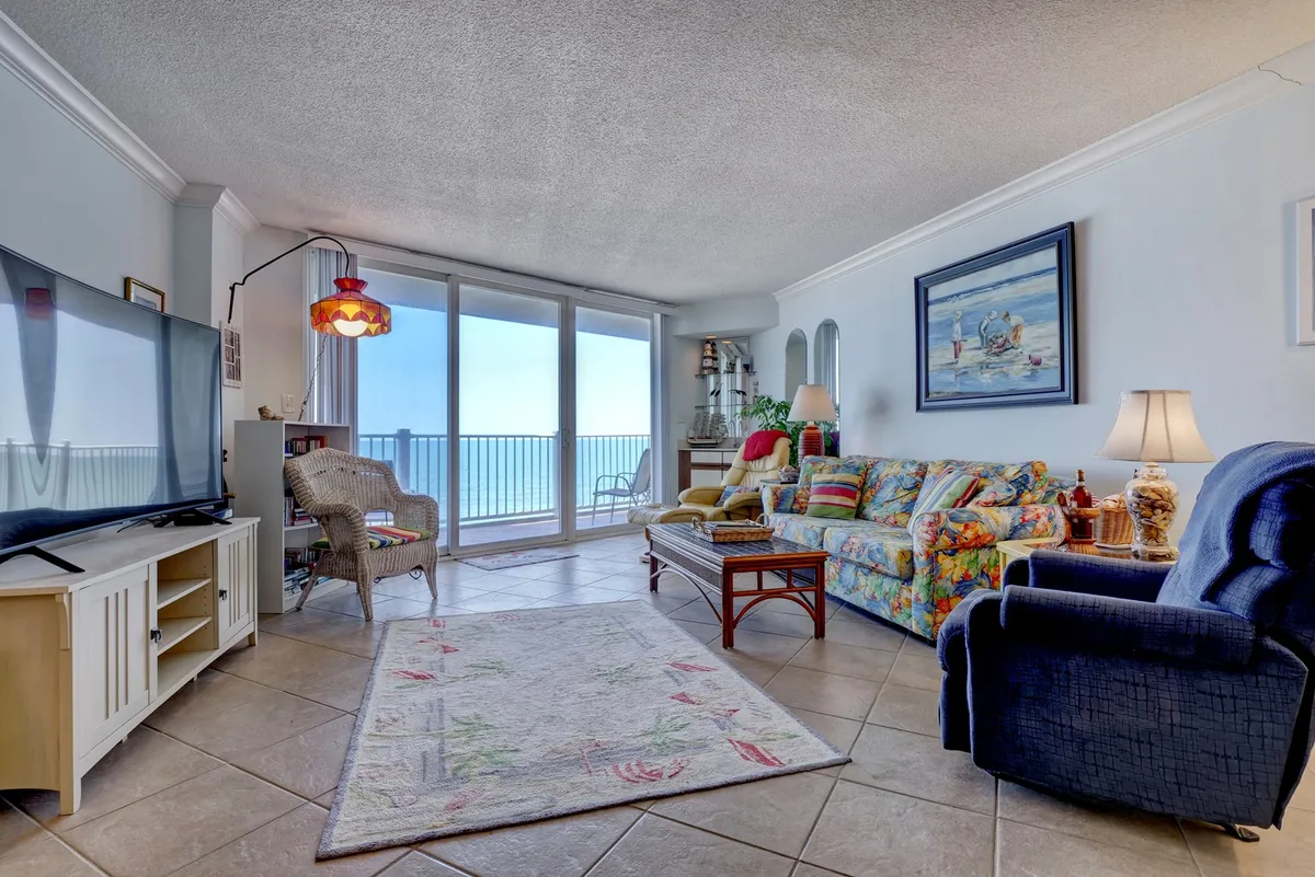 A cheerful living room with a colorful sofa, expansive windows overlooking the Atlantic, and a TV stand. The space is inviting and cozy, designed for relaxing, entertaining, or watching movies while enjoying the endless blue sea.