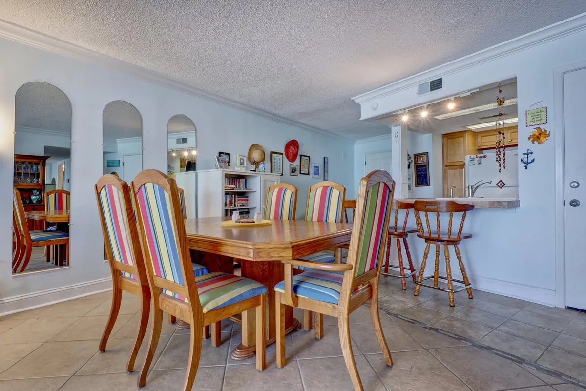 A bright dining table with striped chairs is set within view of the kitchen area and a mirrored wall, providing evidence of a seamless flow between cooking and dining spaces. The mood is cheerful and communal, perfect for shared meals and social gatherings.