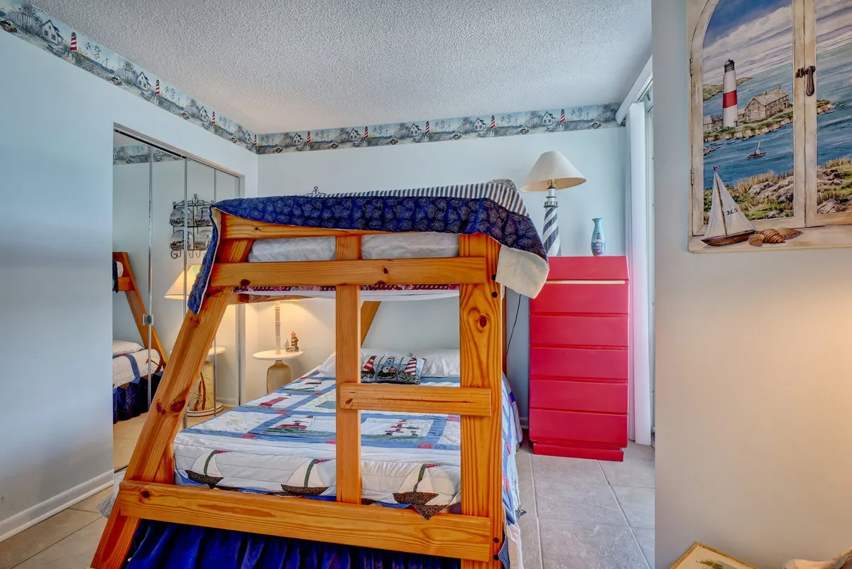 A playful bedroom featuring a bunk bed, red dresser, nautical-themed decor, and a lamp. The room feels inviting for both children and adults, with cozy spaces for reading, playing, or relaxing. Bright tones and playful elements make it a welcoming family space.