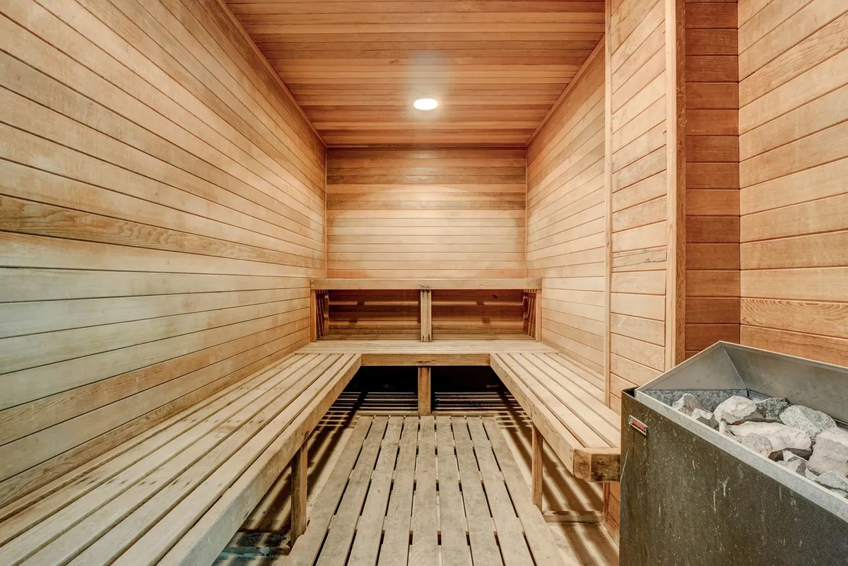 A serene sauna room featuring smooth wooden benches and a central stone heater, with soft lighting inviting guests to unwind and recharge. The clean, tranquil space is ideal for post-workout recovery or relaxation after a day of resort activities.